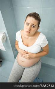 Portrait of upset pregnant woman feeling unwell using toilet