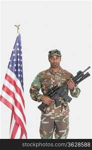 Portrait of US Marine Corps soldier with M4 assault rifle standing by American flag over gray background