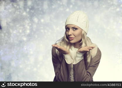 portrait of very pretty young girl with long blonde hair and winter clothes. She wearing wool cap, sweater and warm coat. Blowing on her hands