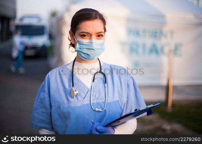 Portrait of very tired   exhausted UK NHS ICU doctor in front of hospital,emergency patient triage tent in background,Coronavirus COVID-19 pandemic outbreak crisis,medical staff working long shifts  