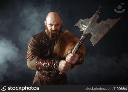 Portrait of viking with axe, martial spirit, barbarian image. Ancient warrior in smoke on dark background. Portrait of viking with axe, martial spirit