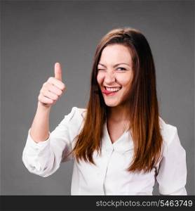 Portrait of winking and smiling business woman with thumbs up, on gray background