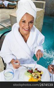 Portrait of woman in bathrobe, eating by pool