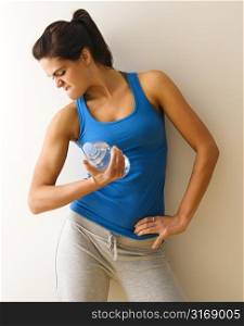 Portrait of woman in fitness attire flexing arm muscle holding water bottle.