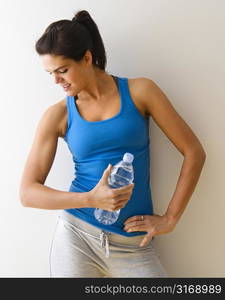 Portrait of woman in fitness attire flexing arm muscle holding water bottle and smiling.