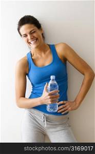 Portrait of woman in fitness attire holding water bottle and laughing.