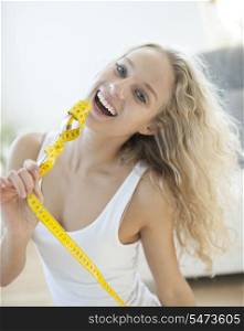 Portrait of woman laughing while holding fork wrapped with measuring tape