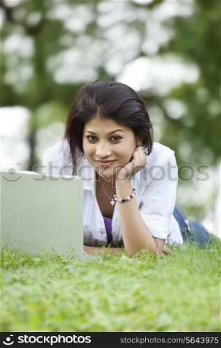 Portrait of woman lying on grass in lawn and using laptop