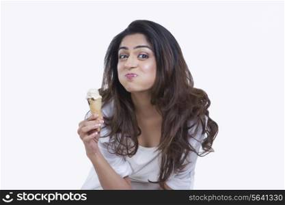 Portrait of woman making face while eating ice cream cone over while background