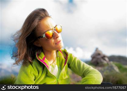 Portrait of woman resting in mountains looking at the sun with glasses.