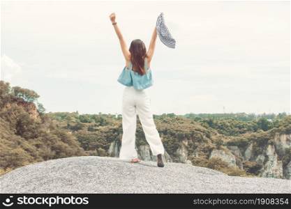 Portrait of woman&rsquo;s back wearing hat travel and raising hands on the top of mountains in summer time with background of blur tree and blue sky