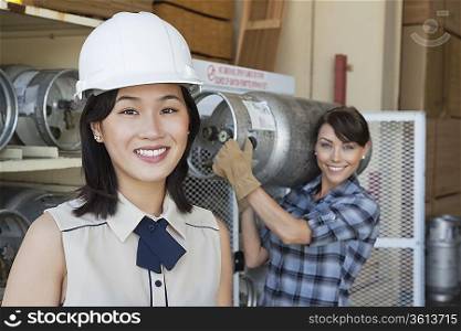 Portrait of woman smiling with female industrial worker carrying propane cylinder in background
