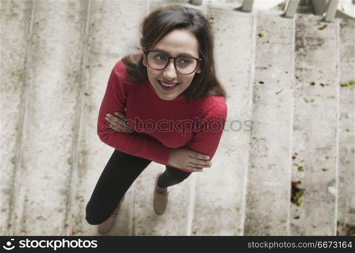 Portrait of woman standing with arms crossed on staircase looking up