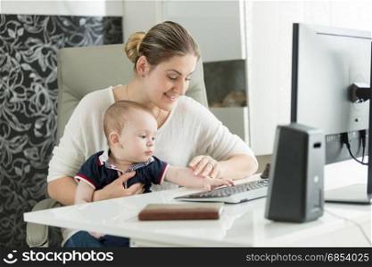 Portrait of woman teaching baby how to use computer