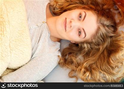 Portrait of woman waking up in bed in the morning after sleeping. Young girl laying under wool blanket.