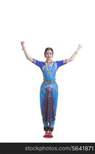 Portrait of woman with arms raised performing Bharatanatyam against white background