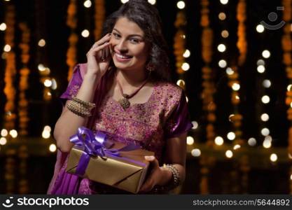 Portrait of woman with gift talking on mobile phone