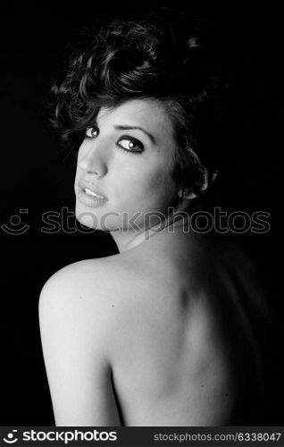 Portrait of woman with intense look on black background, nude shoulder. Studio portrait