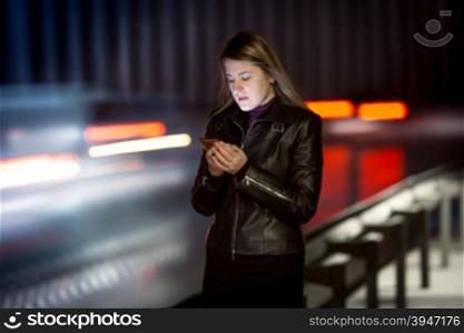 Portrait of woman with mobile phone walking at night next to highway