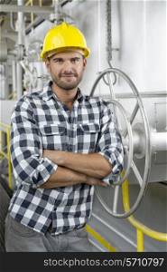 Portrait of worker with arms crossed leaning on large valve in industry