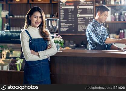 Portrait of young adult asian owner of cafeteria cafe standing in front of barista bar in coffee shop with employee working in background. Using for entrepreneur startup SME concept.