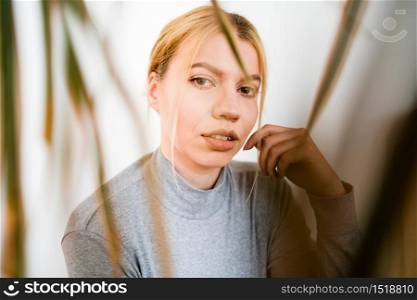 Portrait of young adult caucasian blonde woman looking to the camera trough the plant leaves close up front view Ideas Idyllic fantasy lust and nostalgia concept