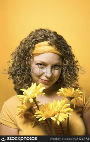 Portrait of young adult Caucasian woman on yellow background holding bouquet of flowers.