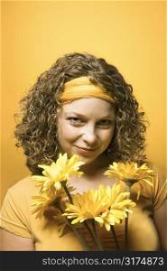 Portrait of young adult Caucasian woman on yellow background holding bouquet of flowers.
