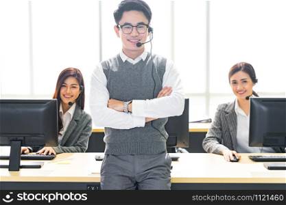 Portrait of Young adult friendly and confidence operator man with headsets and his team working in a call center as customer service and technical support.