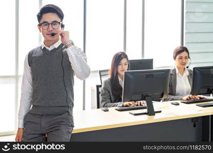 Portrait of Young adult friendly and confidence operator man with headsets and his team working in a call center as customer service and technical support.