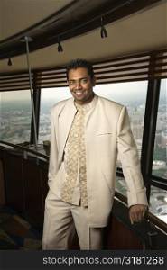 Portrait of young adult male Indian standing near window in tower restaurant smiling at viewer.