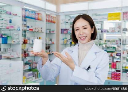 Portrait of young affable pharmacist show qualified medicine pill bottle mockup product for copyspace at pharmacy. Druggist working with her diary job at drugstore, medicine box on shelf at background. Portrait of young asian pharmacist pill bottle mockup at qualified pharmacy
