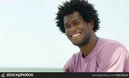 Portrait of young african american guy looking at camera near the sea. Copy space