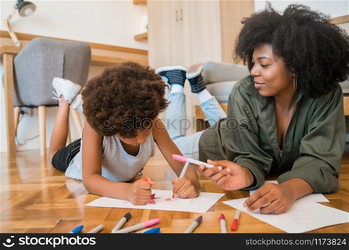 Portrait of young african american mother and son drawing with colored pencils on warm floor at home. Family concept.