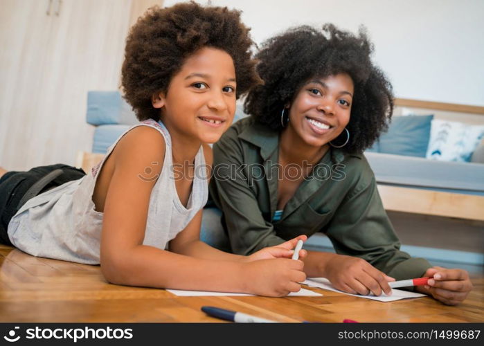 Portrait of young african american mother and son drawing with colored pencils on warm floor at home. Family concept.