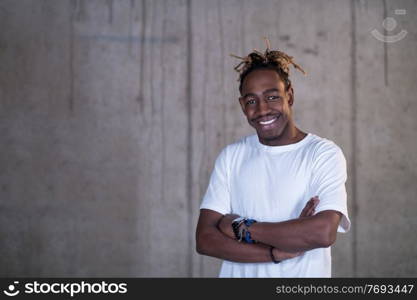 portrait of young african american smiling casual businessman standing in front of a concrete wall at new startup office