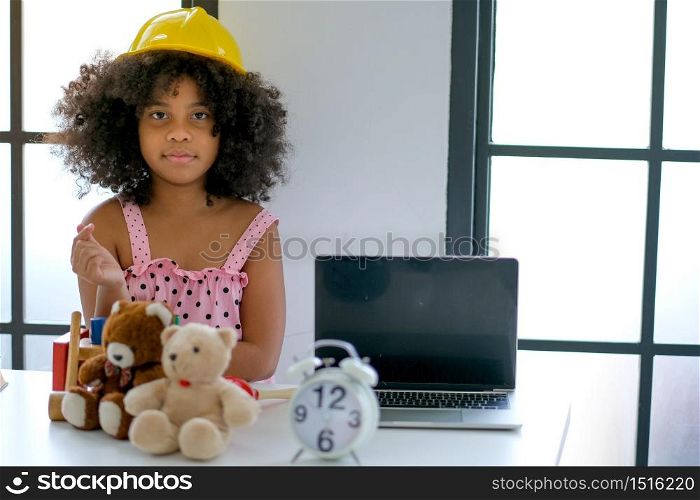 Portrait of young African girl play as engineer by wearing yellow hat in the living room with some decorations.