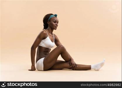 Portrait of young african woman doing stretching exercise on beige background