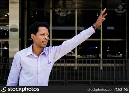 Portrait of young Afro American businessman flagging down a taxi.