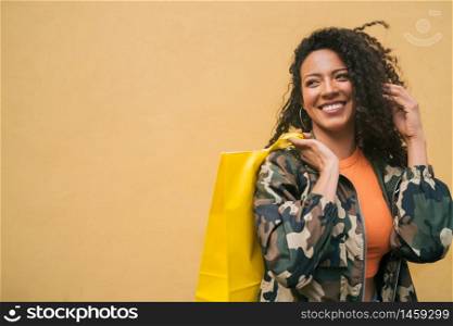 Portrait of young afro american latin woman holding shopping bags against yellow background. Shop and lifestyle concept.