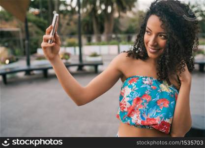 Portrait of young afro american latin woman taking a selfie with mobile phone outdoors in the street.