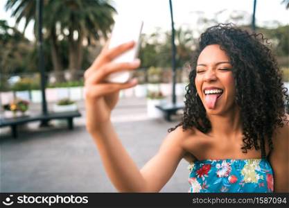 Portrait of young afro american latin woman taking a selfie with mobile phone outdoors in the street.