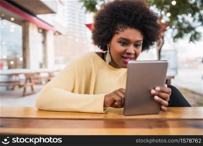 Portrait of young afro american latin woman using her digital tablet while sitting at the coffee shop. Technology concept.