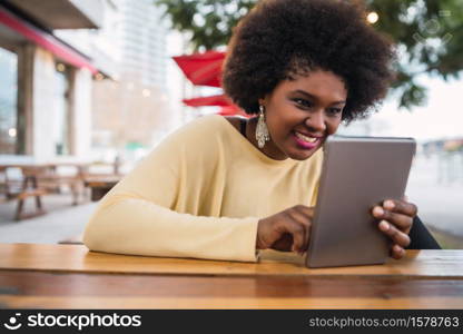 Portrait of young afro american latin woman using her digital tablet while sitting at the coffee shop. Technology concept.