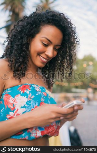 Portrait of young afro american latin woman using her mobile phone outdoors in the street. Technology concept.