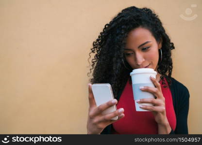 Portrait of young afro american latin woman using her mobile phone while drinking coffee. Technology concept.