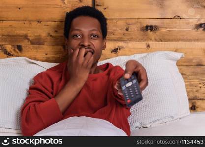 Portrait of young afro american man watching tv and relaxed on bed at home.