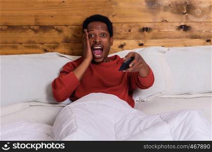 Portrait of young afro american man watching tv and relaxed on bed at home.