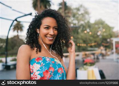 Portrait of young Afro american woman enjoying the day and listening to music with earphones in the street.