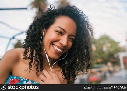 Portrait of young Afro american woman enjoying the day and listening to music with earphones in the street.
